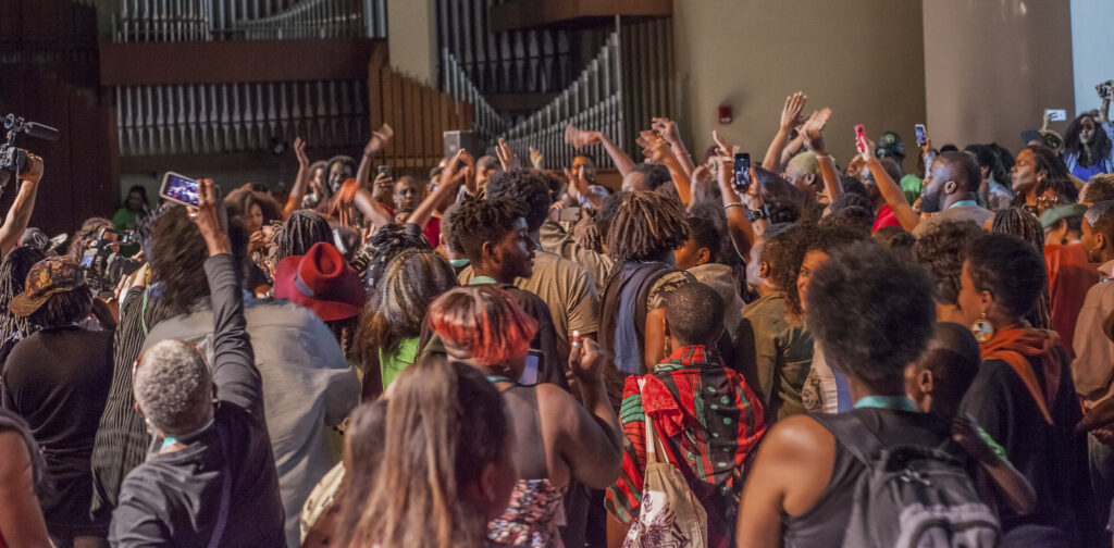 A large group of Black folx joining the stage at the AMC Opening Ceremony, waving their arms in the air