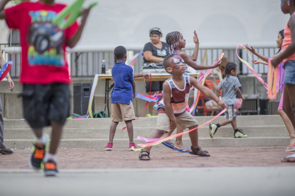 AMC kids playing outside with ribbons and facepaint in front of a DJ