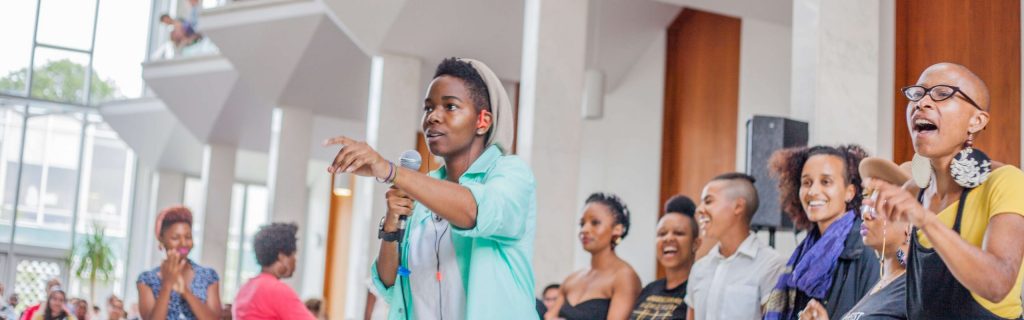 Image of a young Black person standing with a group of people behind them. Everyone is smiling and laughing.